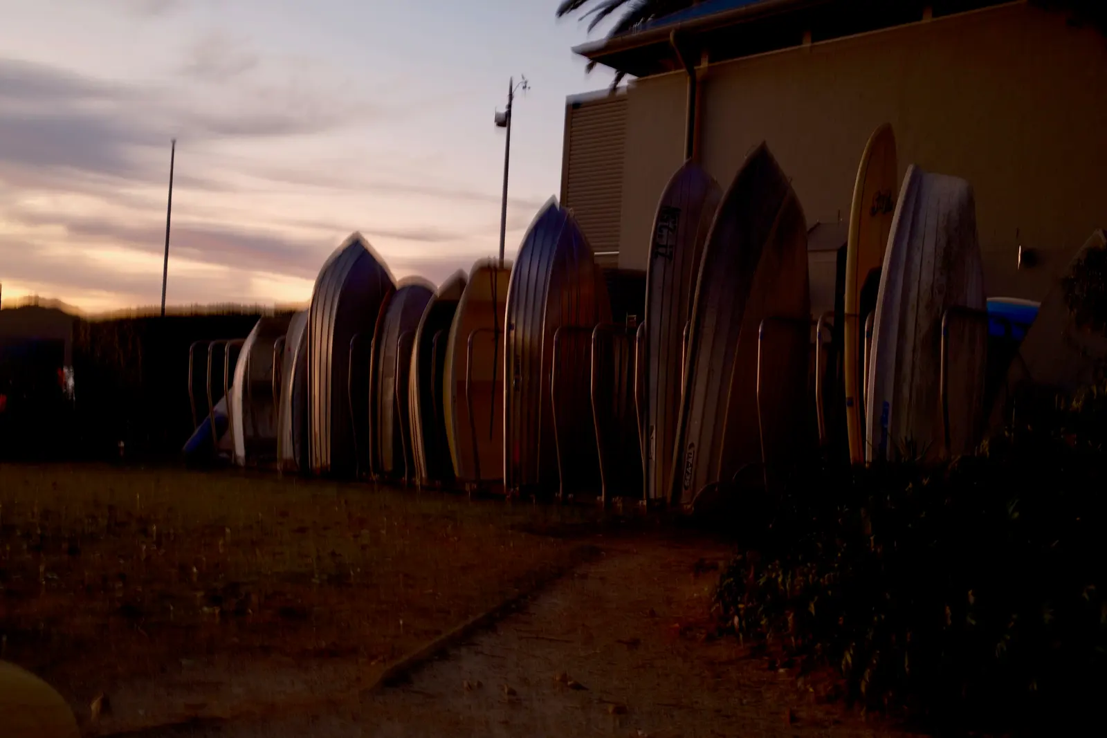Aluminium dinghies stored upright in a row of racks beside a building, against a dusk sky